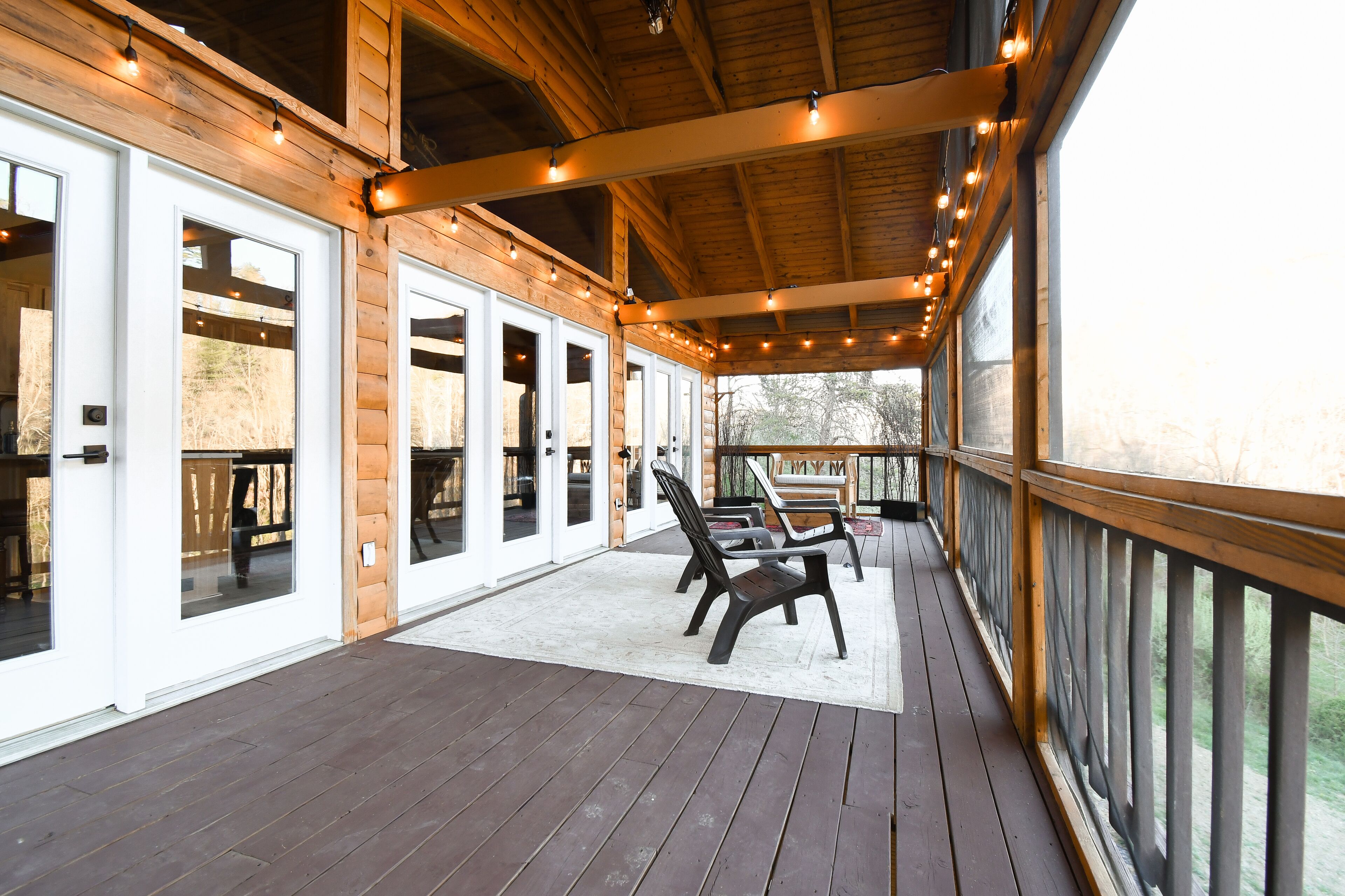 Une terrasse en bois dotée d’un espace couvert, avec une rangée de portes-fenêtres coulissantes et une rangée de chaises.