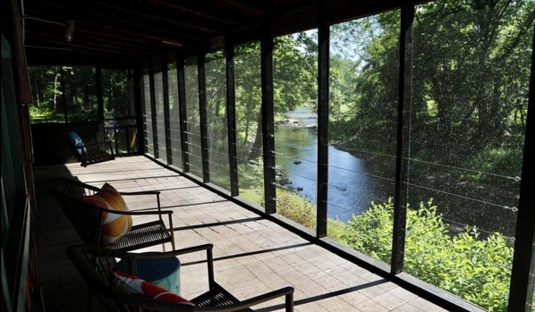 Relax in a serene outdoor space with a river view, surrounded by lush greenery and comfortable seating.