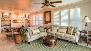 A spacious living room with a large sofa, a coffee table, and a dining area with a kitchen in the background. - St James Golf Resort-Luxe 3/3 Condo, Sleeps8, Pool, 1DogOk, Gated (St. James Bay)