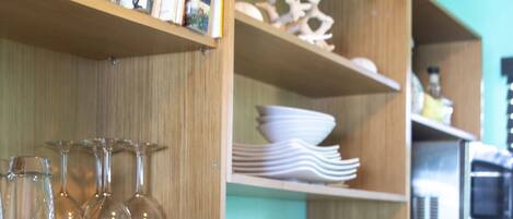Una cocina con estantes de madera que sostienen libros, vasos y utensilios de cocina.