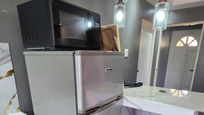 A compact kitchen with a refrigerator, microwave, and a built-in oven. There is a wooden cabinet and a marble countertop. - Cozyville in the Manor (Ocho Rios)