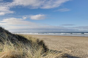 A beach with sand and waves, and some grass in the foreground. - Rockaway Beach Apt w/ Ocean Views: Steps to Shore (Rockaway Beach)