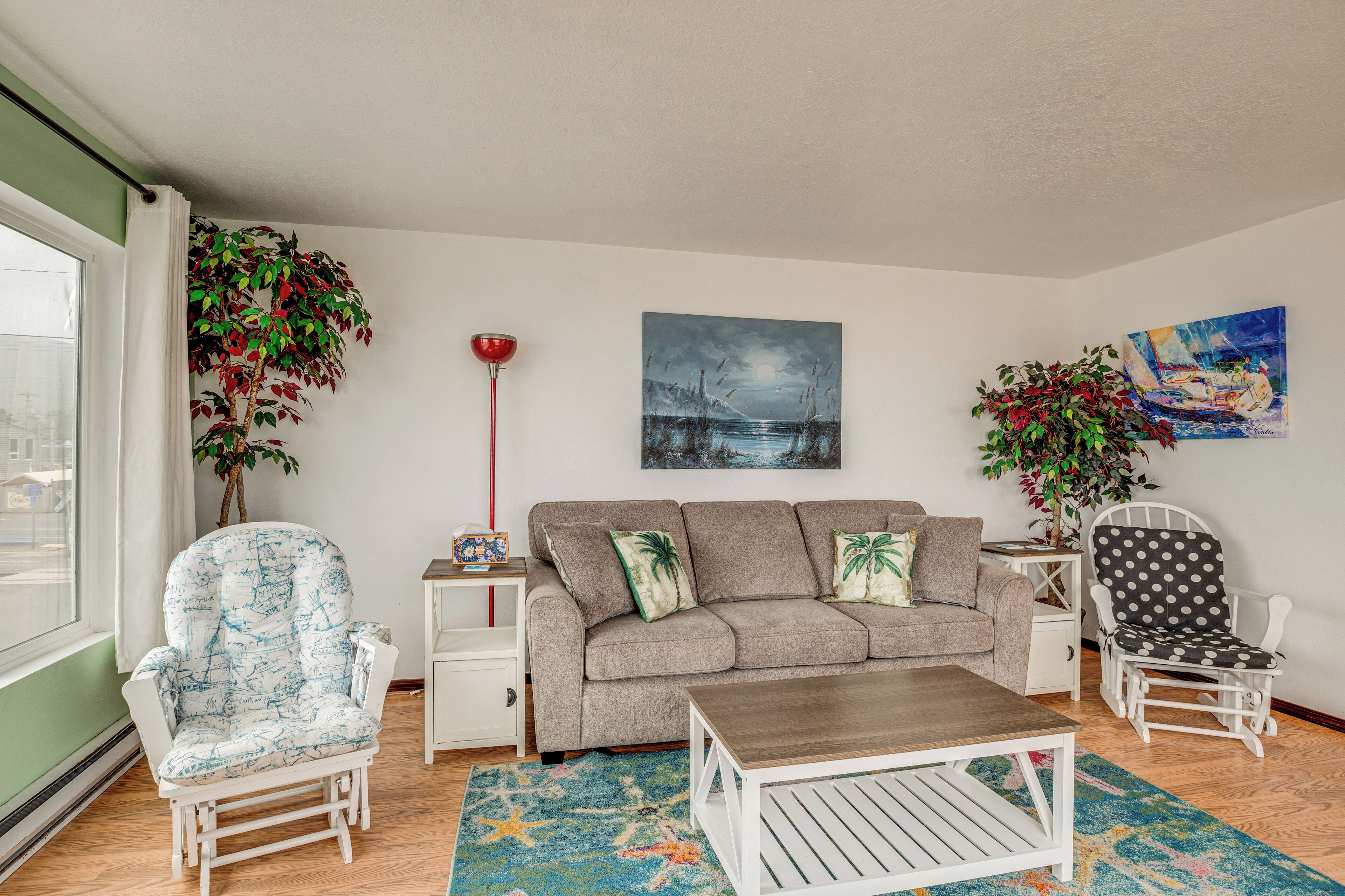 Un salon comprenant un canapé, deux fauteuils, une table basse et deux petites tables d’appoint. Deux plantes en pot sont disposées de part et d’autre du canapé. Un tableau est accroché au mur, au-dessus du canapé.