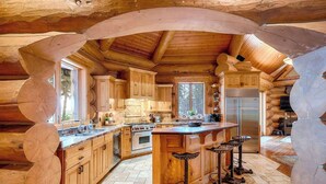 A log cabin kitchen with wooden cabinets, a central island, bar stools, a stove, and a refrigerator.