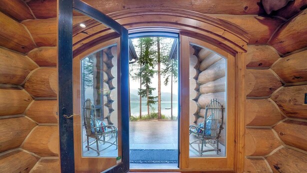 A log cabin interior with a large wooden door leading to a porch with two rocking chairs.