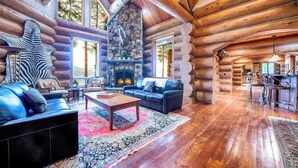 A log cabin interior with a fireplace, wooden floors, and a cozy seating area.