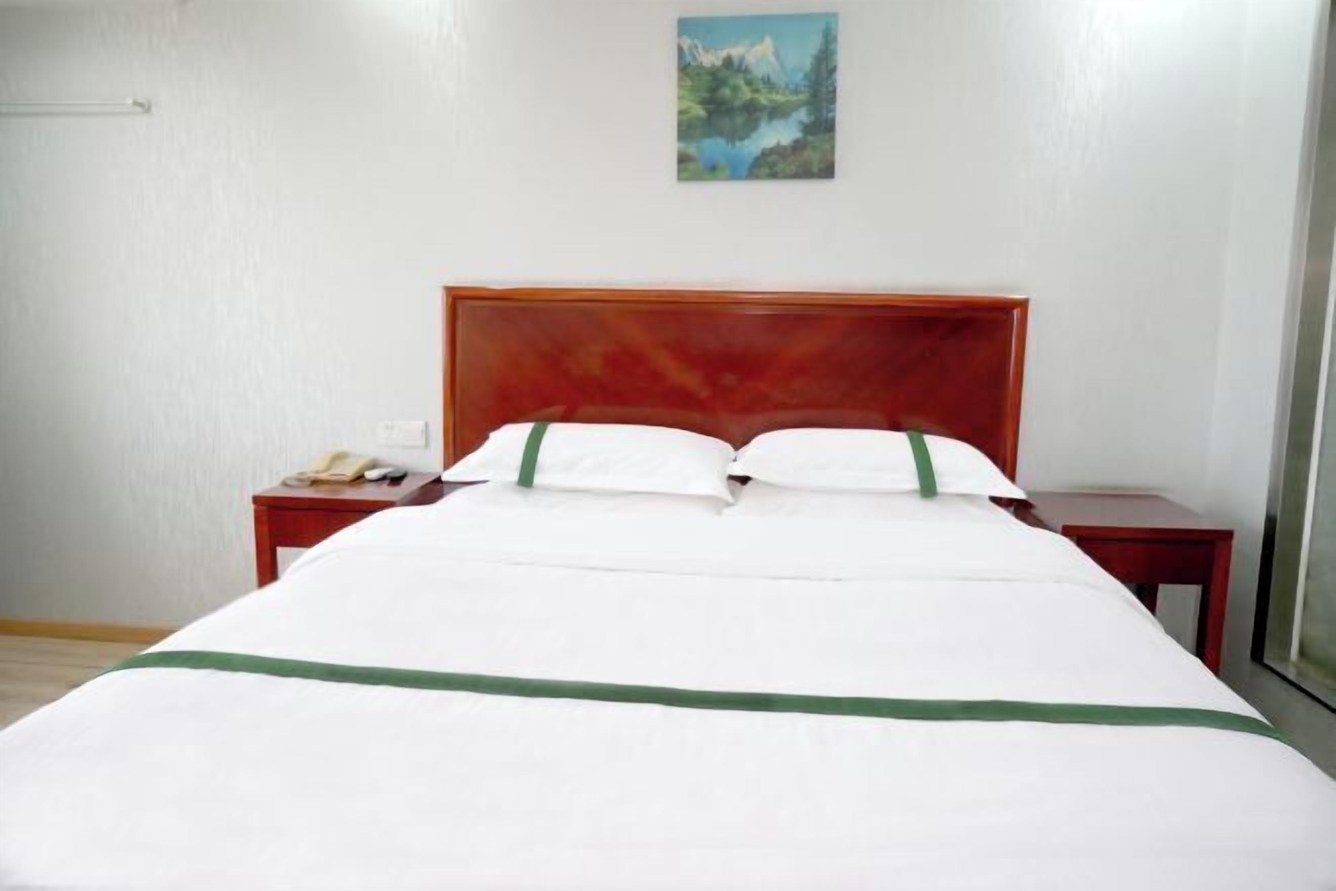 Un lit bien fait, avec une tête de lit en bois, une table de chevet sur laquelle se trouve un téléphone, et un tableau accroché au mur.