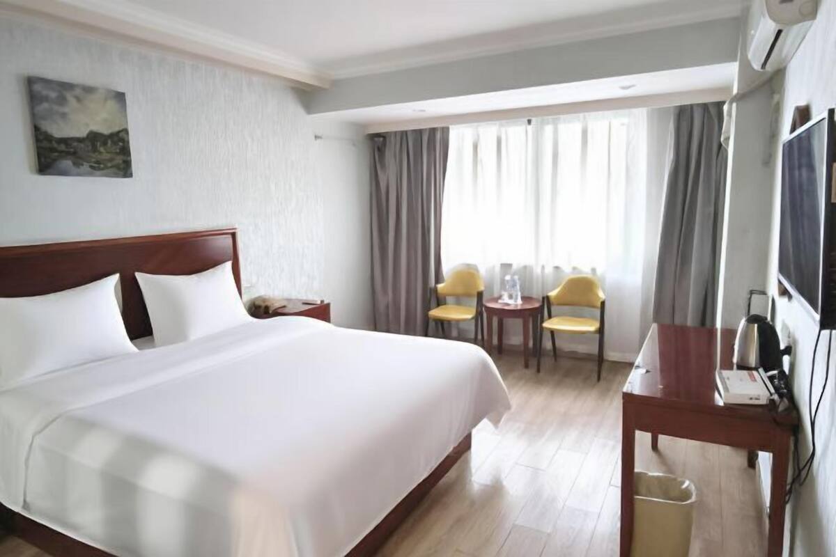 A hotel room with a large bed, a desk with a chair, a TV, and a window with curtains.