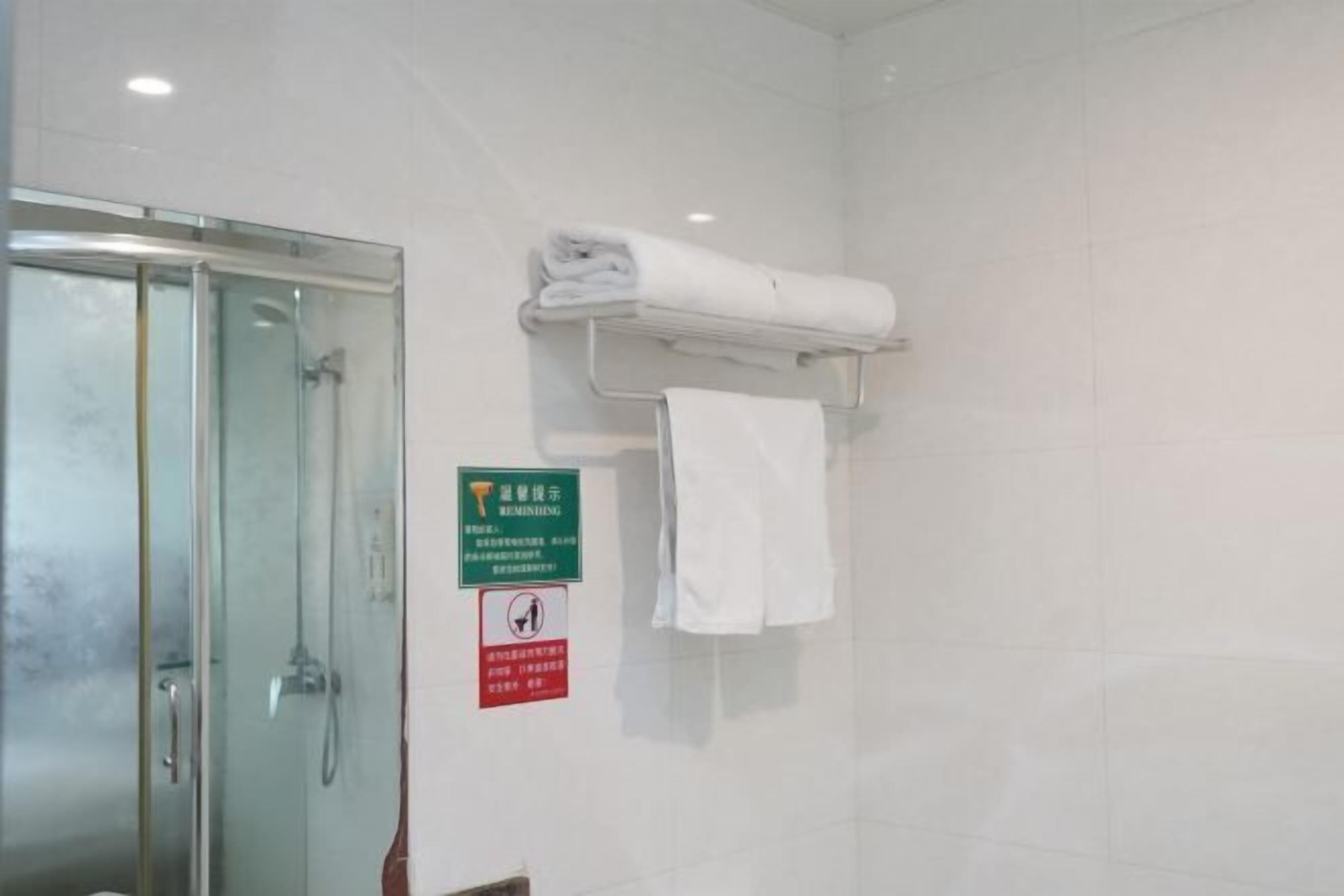 A bathroom with a glass shower enclosure, a towel rack with folded towels, and two signs on the wall.