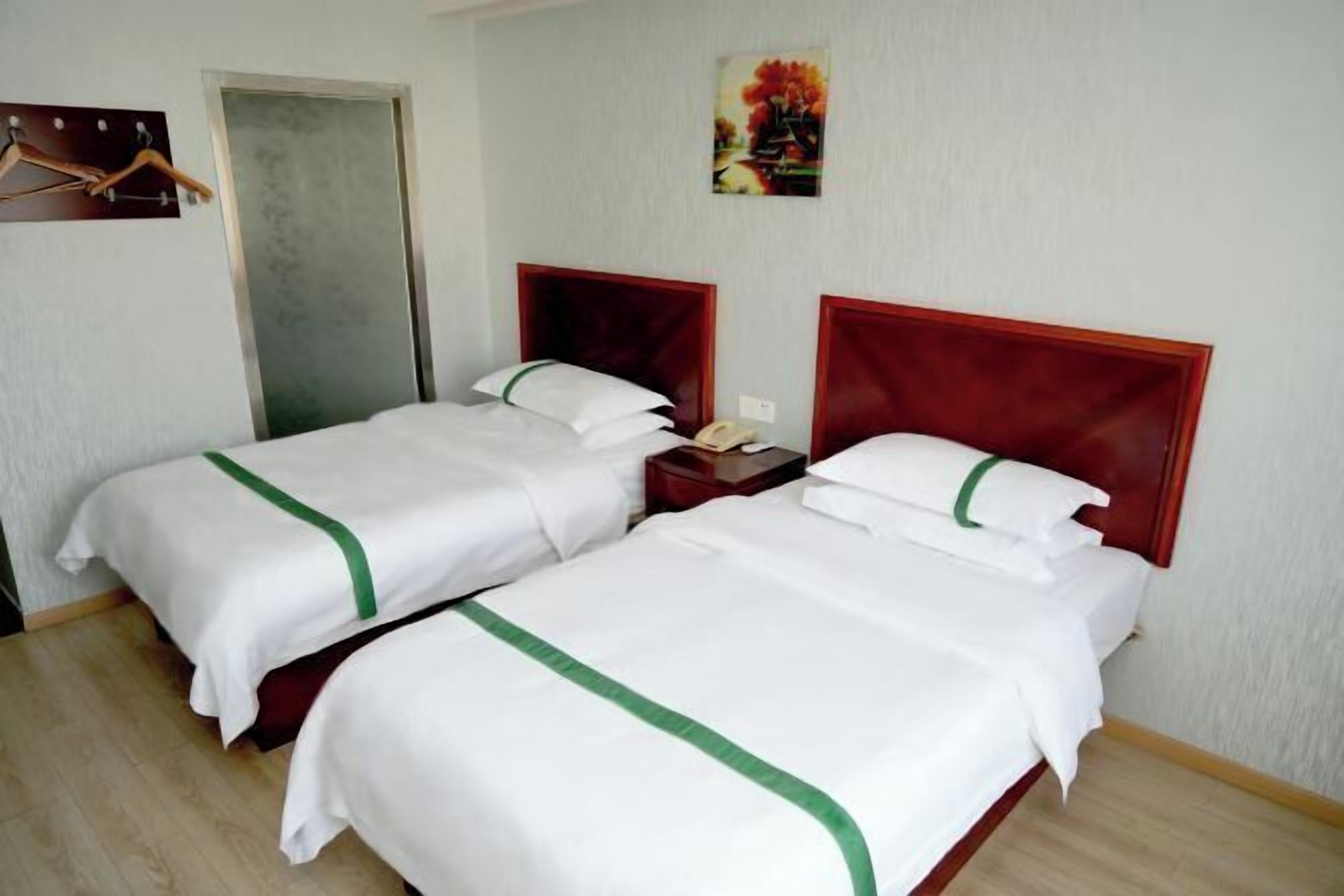A hotel room with two beds, a wooden floor, a door, and a wall-mounted artwork.