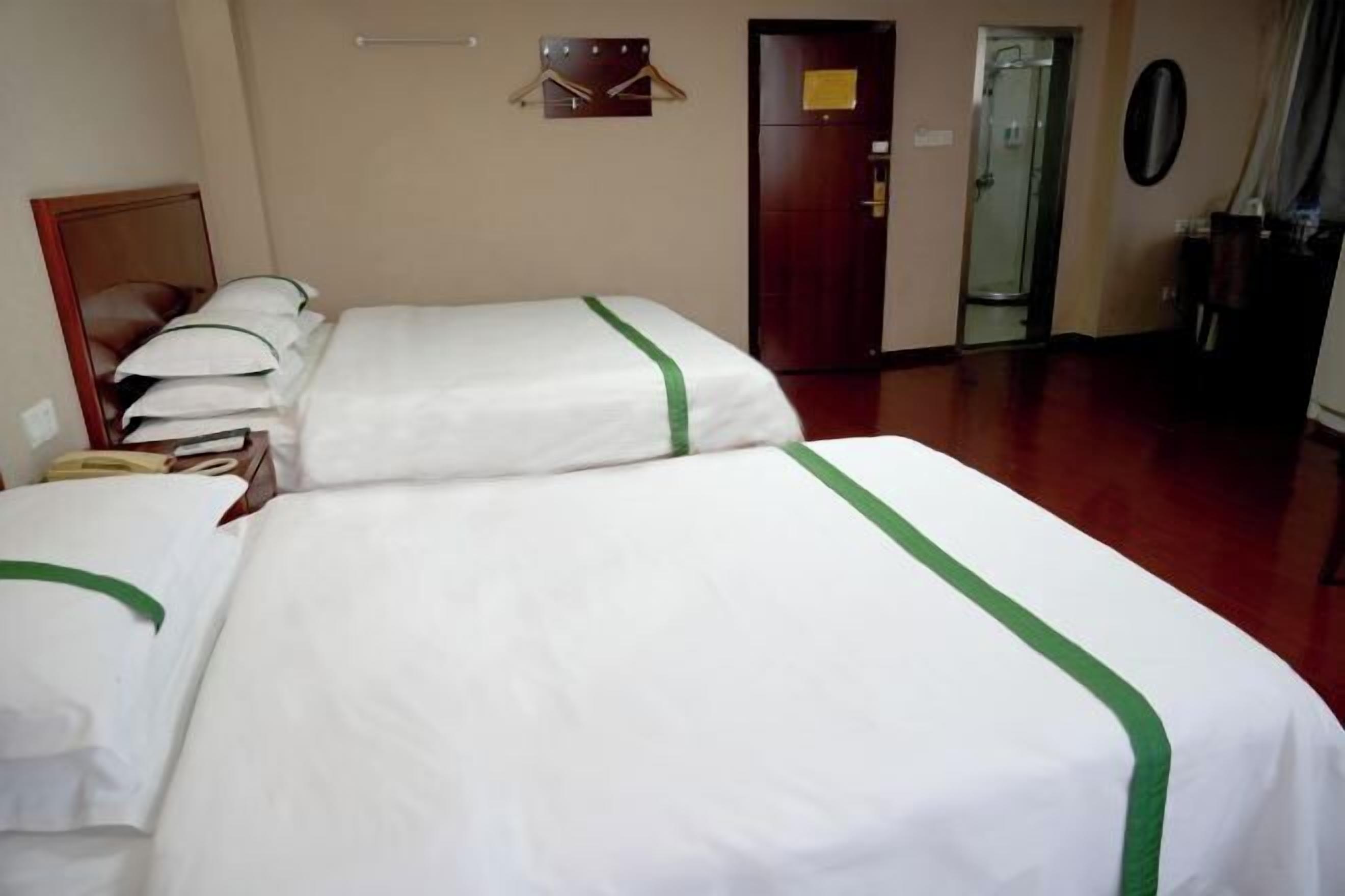 A hotel room with two beds, a wardrobe, a mirror, a coat rack, and a door leading to a bathroom.