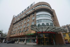 Een meerlaags hotel met een gebogen gevel, een overdekte ingang en diverse winkels op de begane grond.
