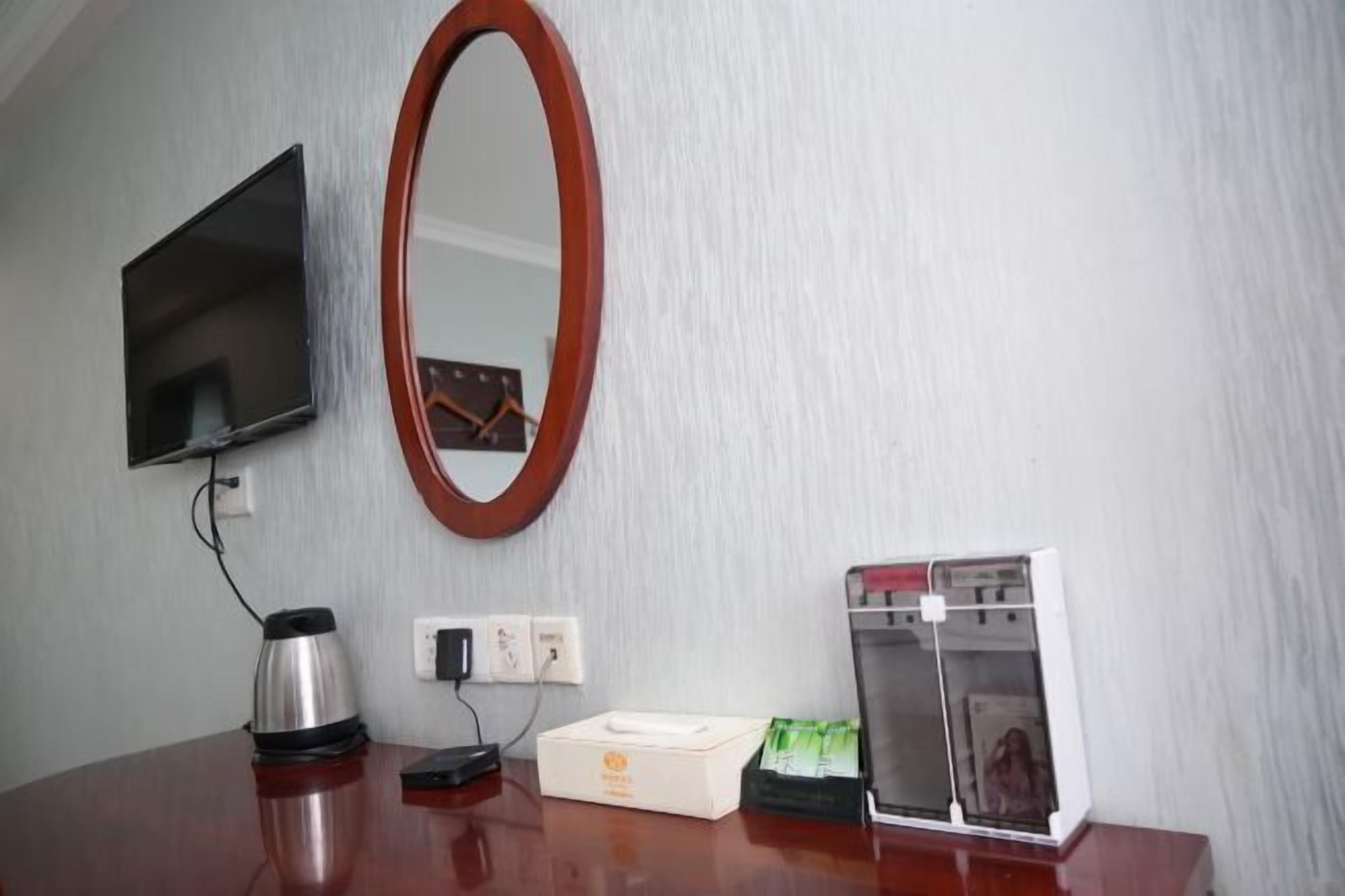 A room with a flat-screen TV mounted on the wall, a round mirror, a coffee maker, a tissue box, and a refrigerator.