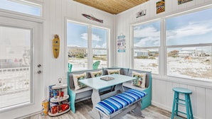 A beach-themed room with a bench, table, and large windows overlooking the beach.