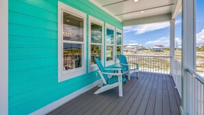A turquoise house with a wooden deck, two blue Adirondack chairs, and a view of the beach.