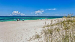 A beach with clear turquoise waters, a sandy shore, and sparse vegetation.