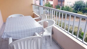 A balcony with a table and chairs, a railing, and a view of neighboring buildings and greenery.