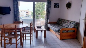 A room with a wooden dining table, chairs, a sofa, and a TV on the wall.