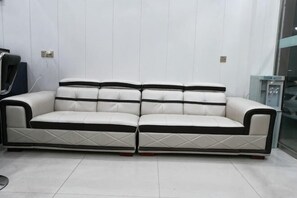 Um sofá de couro branco com detalhes em preto em um quarto com paredes brancas e uma porta de vidro.