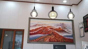 Un área de recepción con un cuadro grande de un paisaje montañoso, iluminación colgante y un mostrador de recepción.