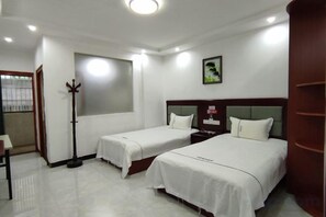 Une chambre d’hôtel avec deux lits, une table de chevet, une fenêtre et un porte-manteau.