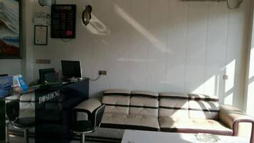 A room with a sofa, a small table, a desk with a computer, and a wall-mounted clock.
