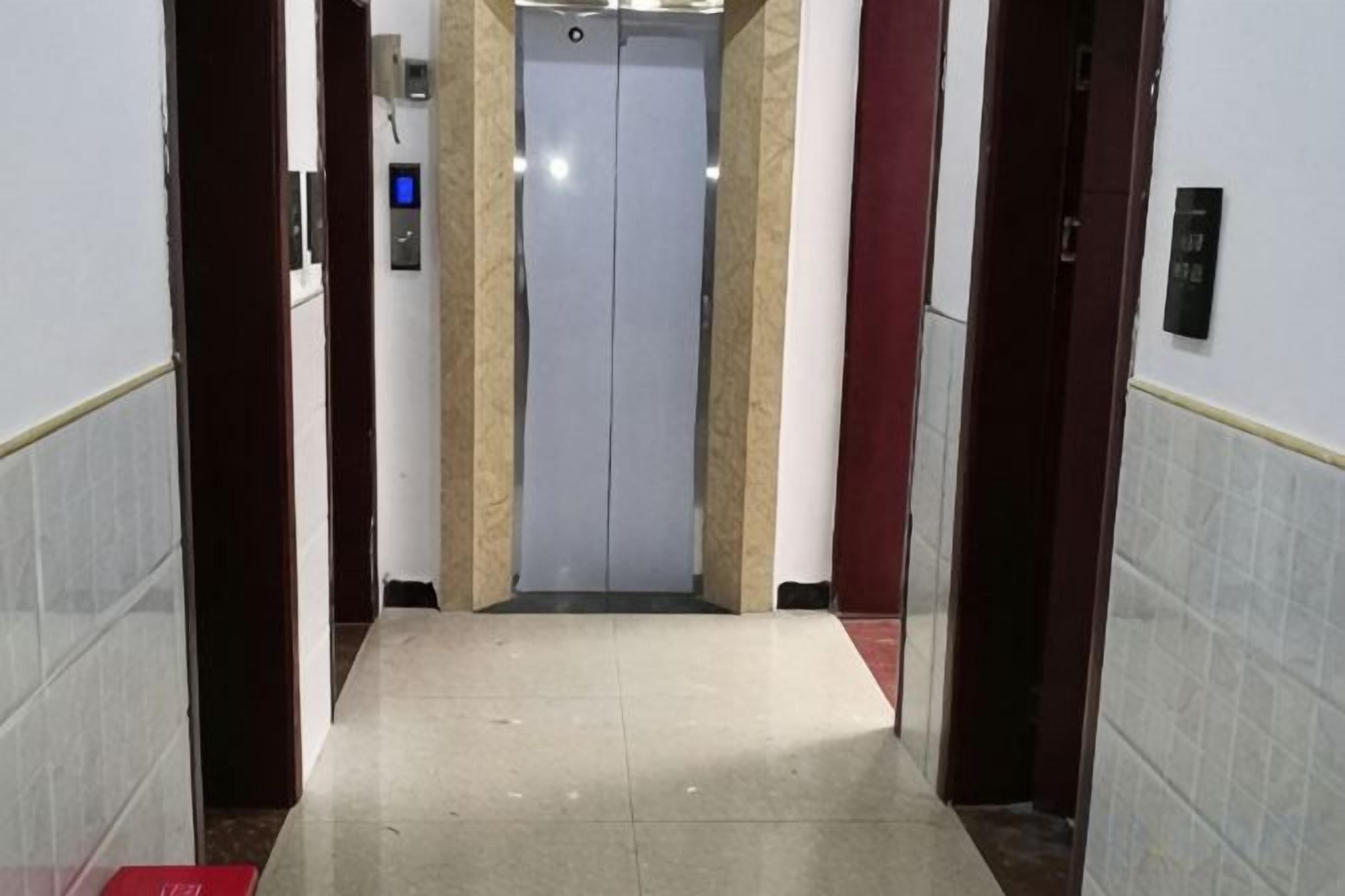 Un corridoio con un ascensore, una porta rossa e un quadro comandi a parete.
