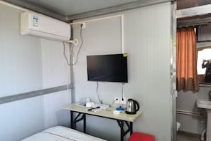 Ein kleines Hotelzimmer mit einem Bett, einem kleinen Tisch mit Fernseher, einem Wasserkocher und einem roten Sessel.