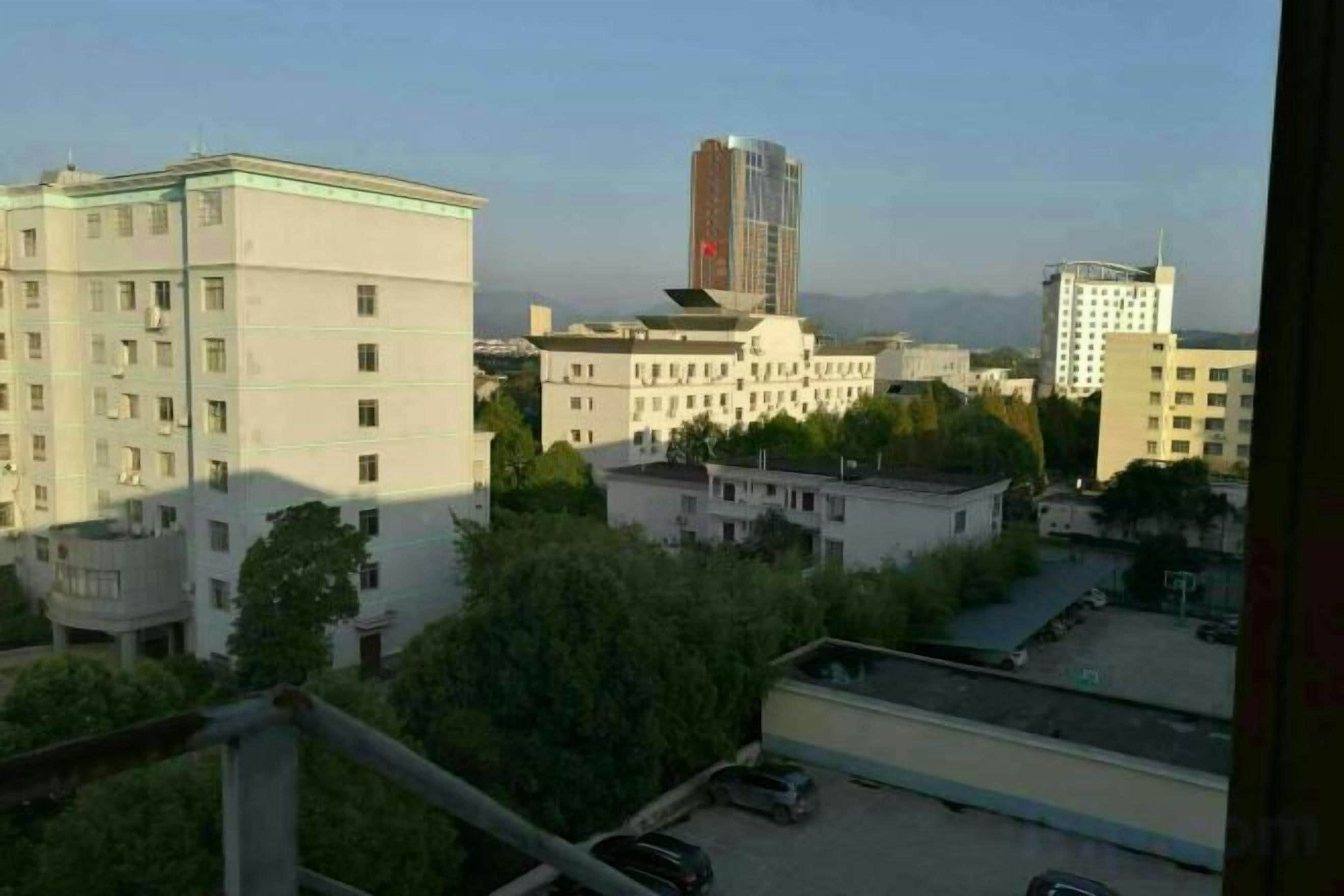 A view of a cityscape with buildings, including a tall structure with a red top, and a parking area with cars.
