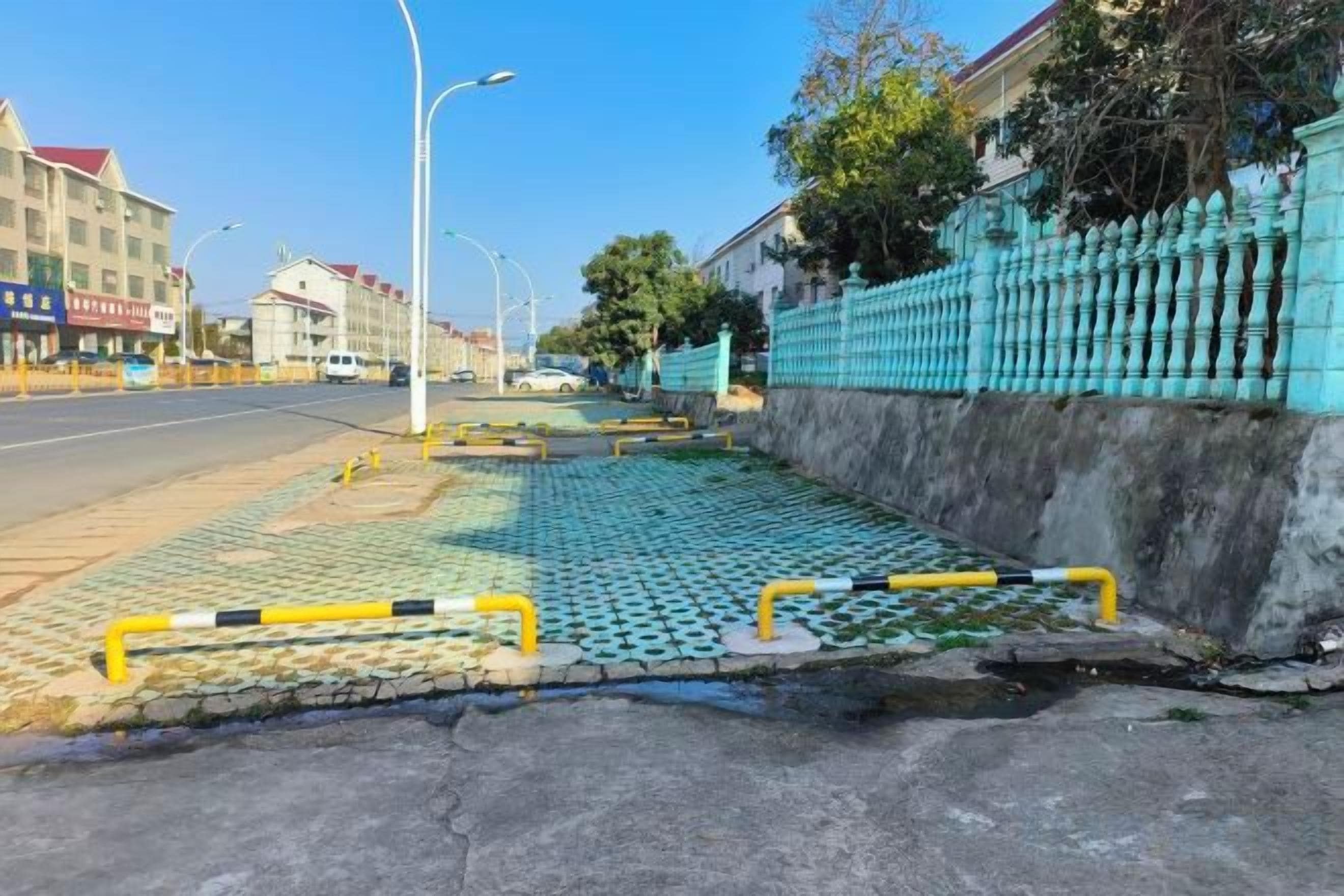 Una calle con acera, una valla azul y un edificio con techo rojo.