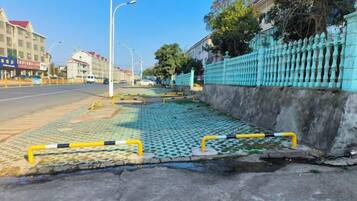 Una calle con acera, una valla azul y un edificio con techo rojo.