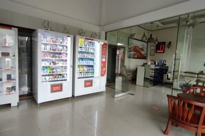 Interior limpo com máquinas de venda automática, divisória de vidro e uma cadeira de madeira.