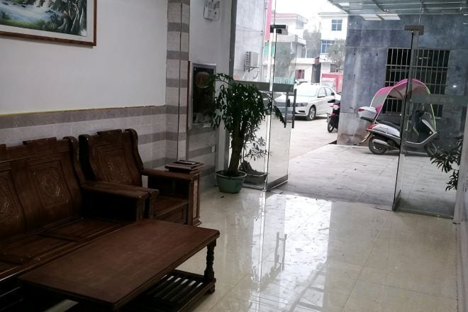 A reception area with a wooden bench, a potted plant, and a glass door leading outside.