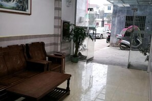 A reception area with a wooden bench, a potted plant, and a glass door leading outside. - Huachen Business Hotel (Wan'an)