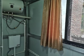 Ein Zimmer mit Heizkörper, Fenster mit Blick auf eine Backsteinmauer und einem Vorhang.