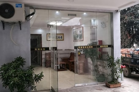 A hotel entrance with glass doors, a reception desk inside, and potted plants outside.. Huachen Business Hotel