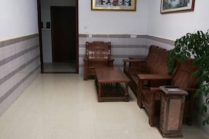 Een kamer met een bank, een houten tafel en een stoel. Er is een deur die naar een andere kamer leidt.