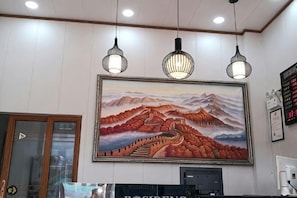 A hotel reception area with a large painting of a mountainous landscape, pendant lighting, and a digital display board. - Huachen Business Hotel (Wan'an)