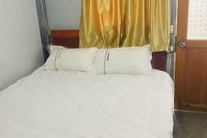 Ein Bett mit weißer Bettwäsche, zwei Kissen, einem Holzkopfbrett und einem gelben Vorhang.