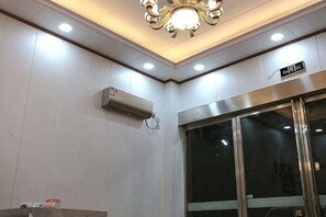 A hotel lobby with a modern ceiling design, a glass elevator, and an air conditioning unit. - Huachen Business Hotel (Wan'an)