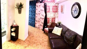 A living room with a dark leather sofa, a patterned curtain, a wall clock, and a small plant. - Nice clean apartment 5 minutes from subway (Toronto)