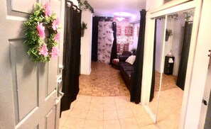 A hallway with a mirror, a door with a floral wreath, and a patterned curtain.