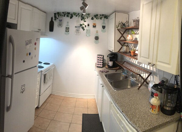A compact kitchen with white cabinets, a refrigerator, a stove, a coffee maker, and a sink.