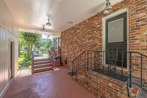 A covered walkway leading to a brick building with a door and window, a staircase, and outdoor greenery.