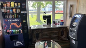 A room with a vending machine stocked with snacks, a coffee machine, and an ATM. - Budget Host Inn (Gilman)