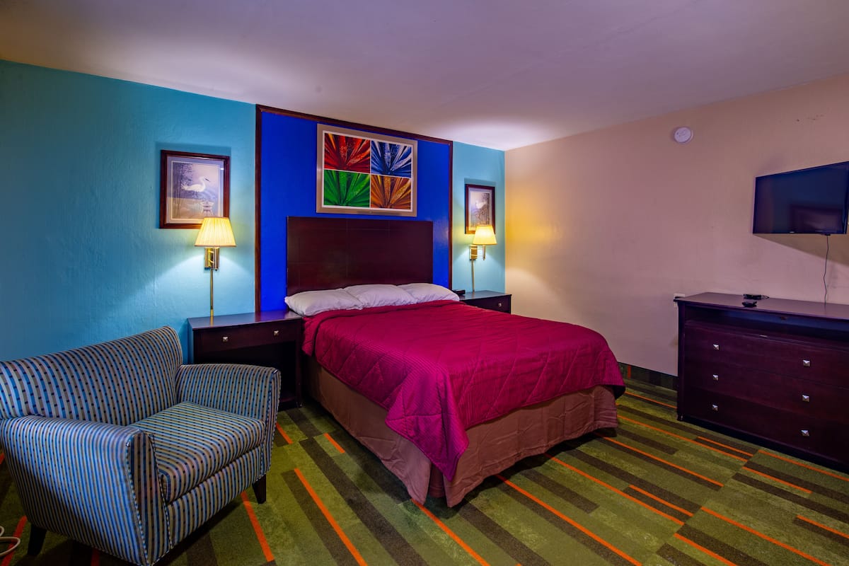 A hotel room with a bed, a chair, a dresser, and two wall-mounted lamps.