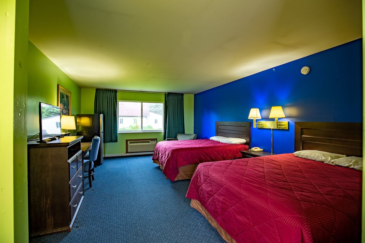 A hotel room with two beds, a desk, a chair, and a window with curtains.