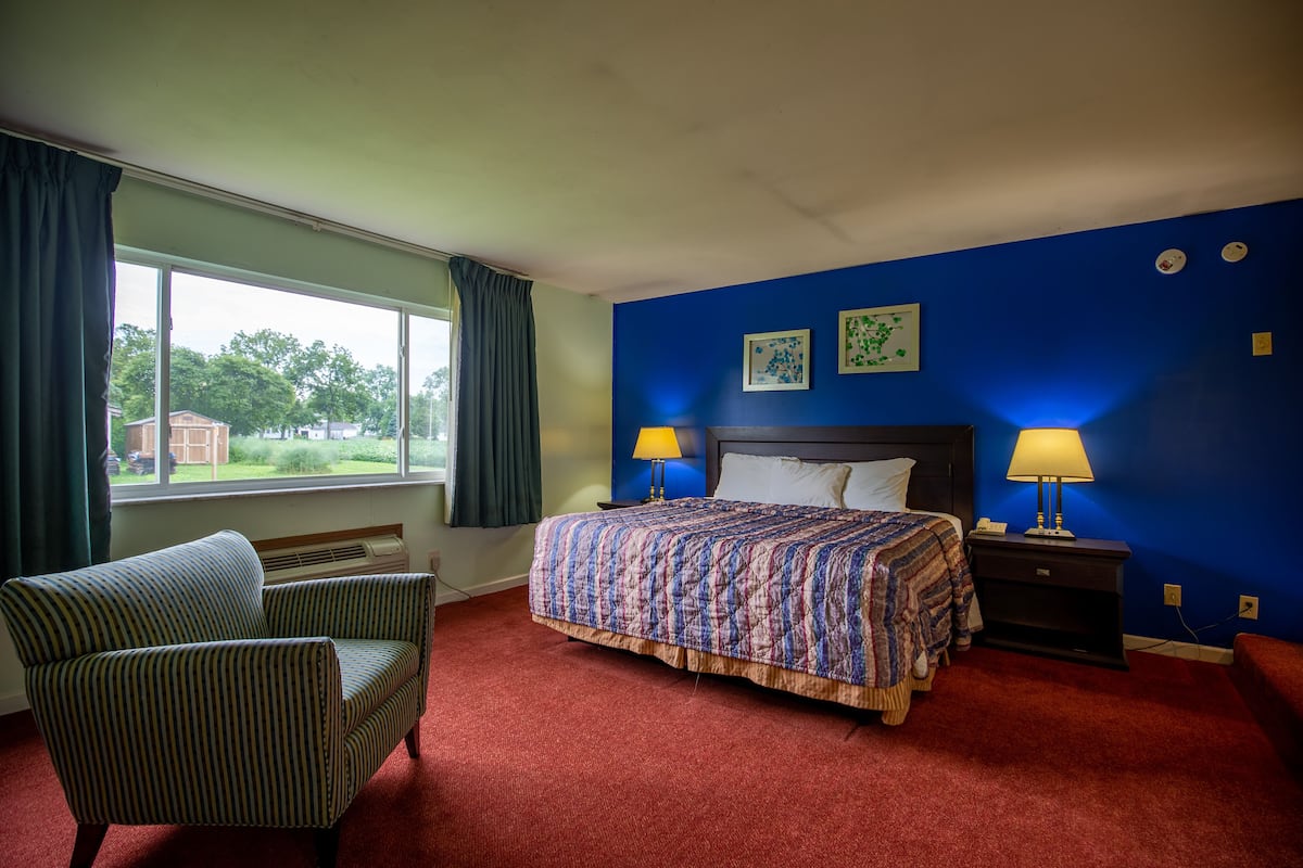 A hotel room with a bed, a chair, a window with curtains, and two wall-mounted lamps.