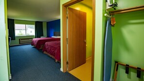 A hotel room with two beds, a wooden door, a radiator, and a window with curtains. - Budget Host Inn (Gilman)
