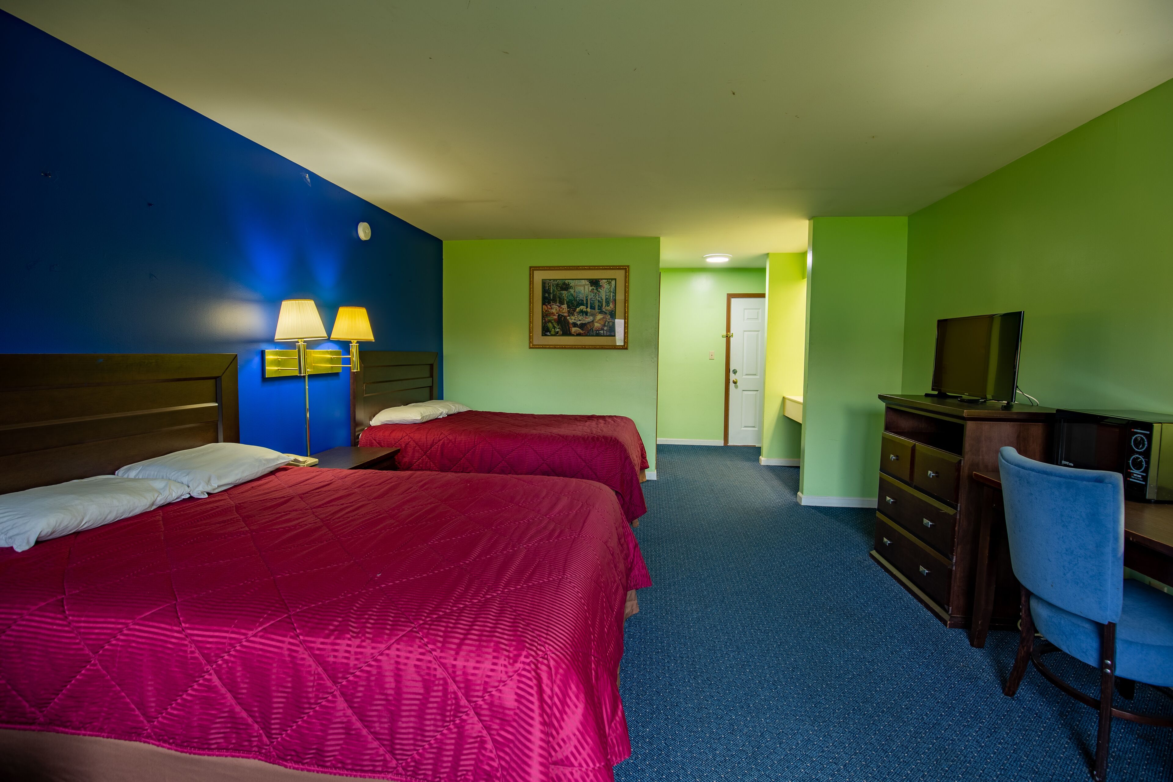 A hotel room with two beds, a desk, a chair, a dresser, a TV, and a painting on the wall.